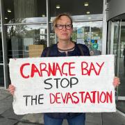 Gill Scott Anderson, of St Ives Climate Coalition, held her sign up behind hotel owner Stephen Baker as he addressed the planning committee (Pic: LDRS)