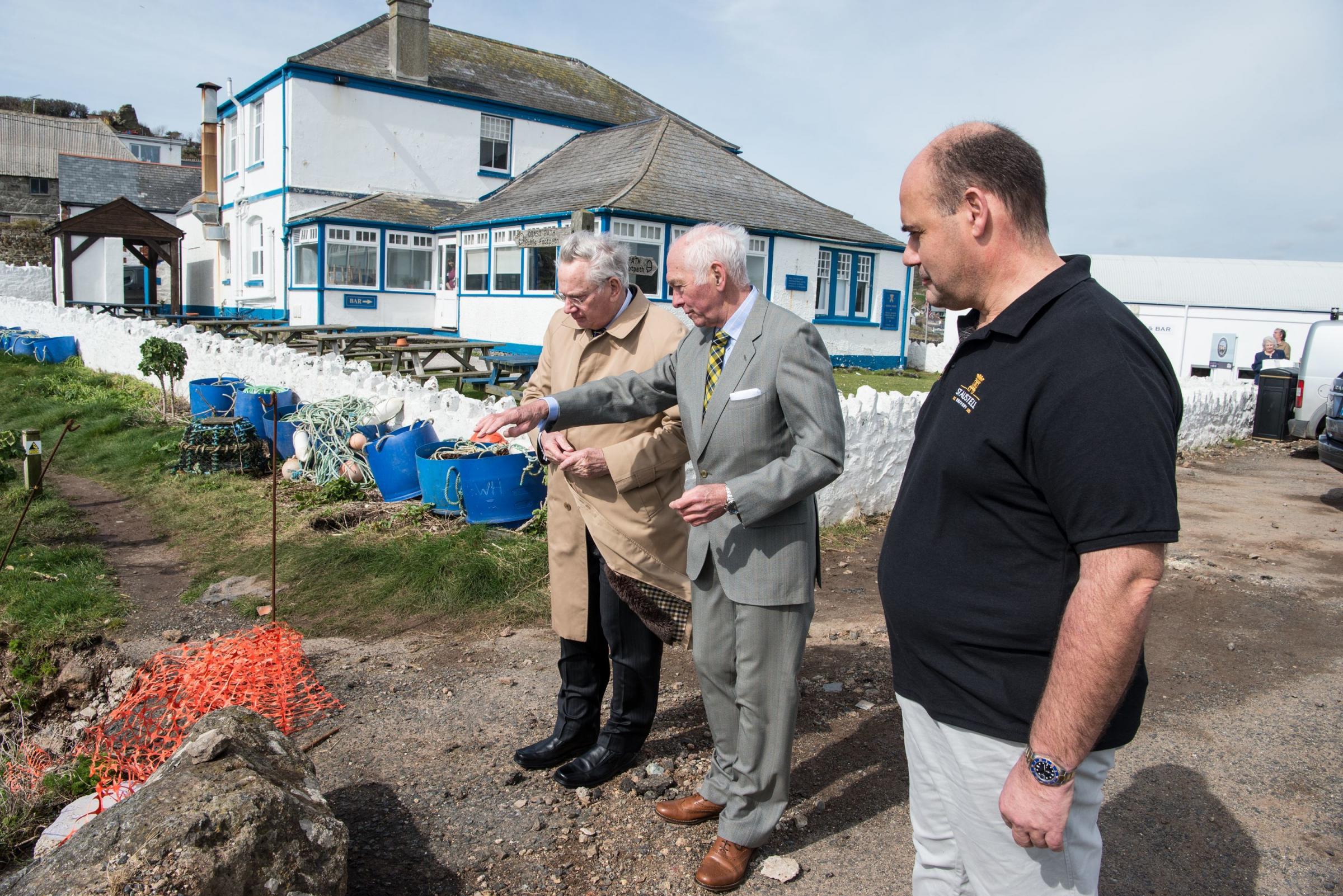 n Bill Frisken of St Keverne Parish Council shows the Duke of Gloucester the damage to the sea wall, watched by Ian, a year after the 2017 flash flood