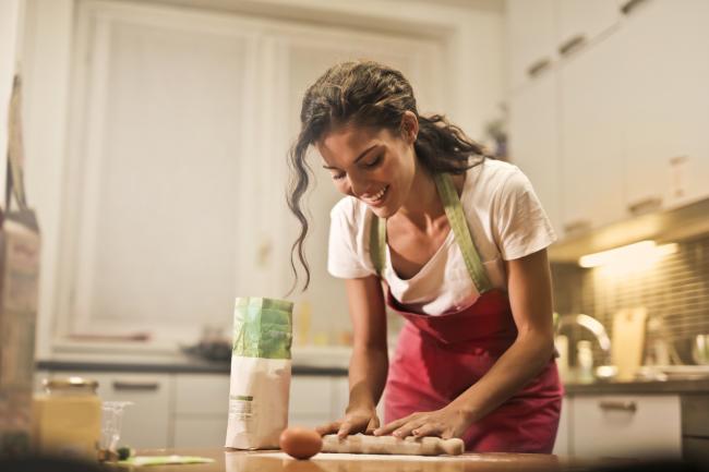 A woman using a rolling pin in her kitchen. Credit: Canva