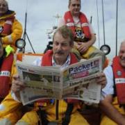Actor John Challis reads a copy of the Helston Packet as he joins the crew of the Lizard lifeboat on the water.